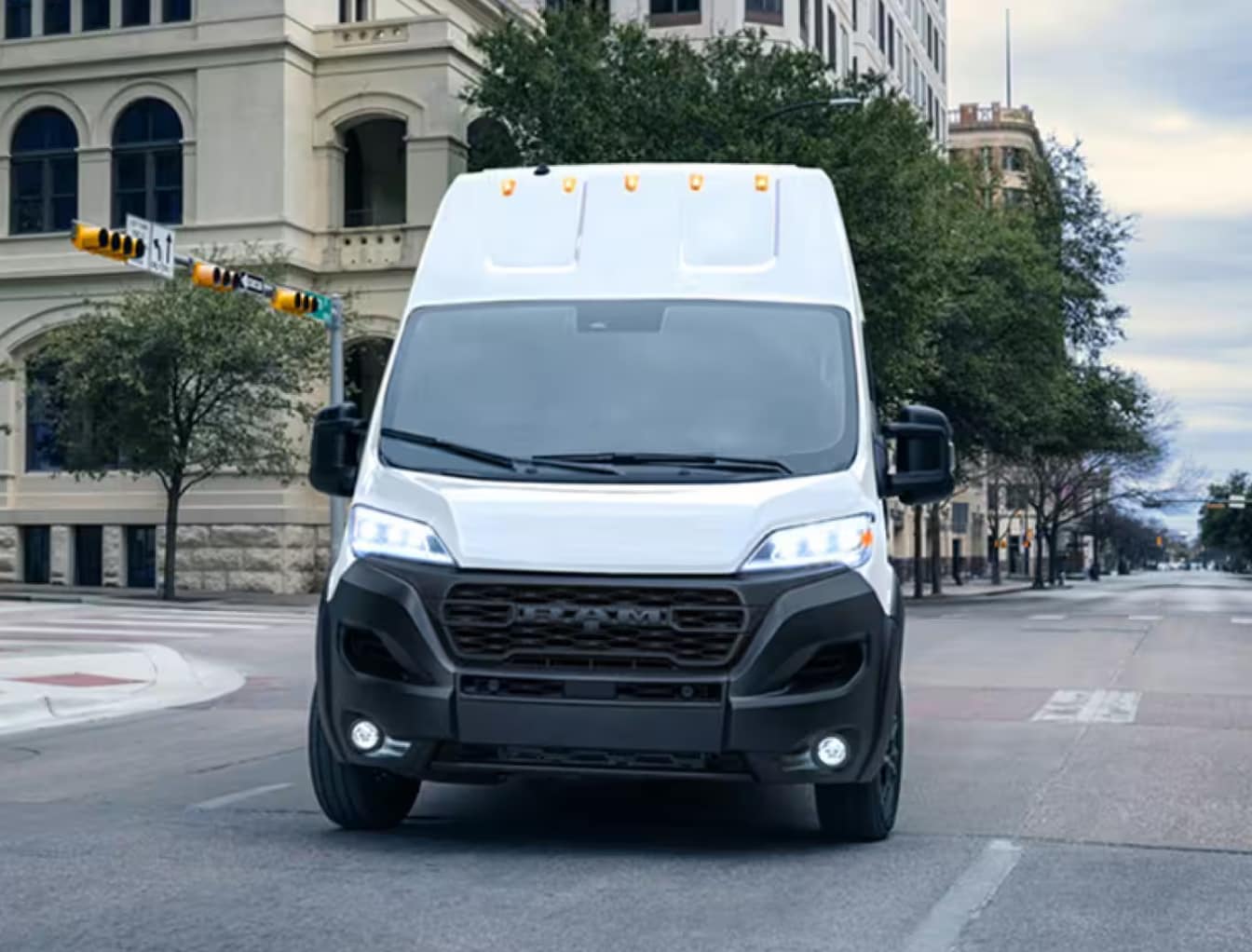 A white Ram Promaster 3500 drives on a city street.