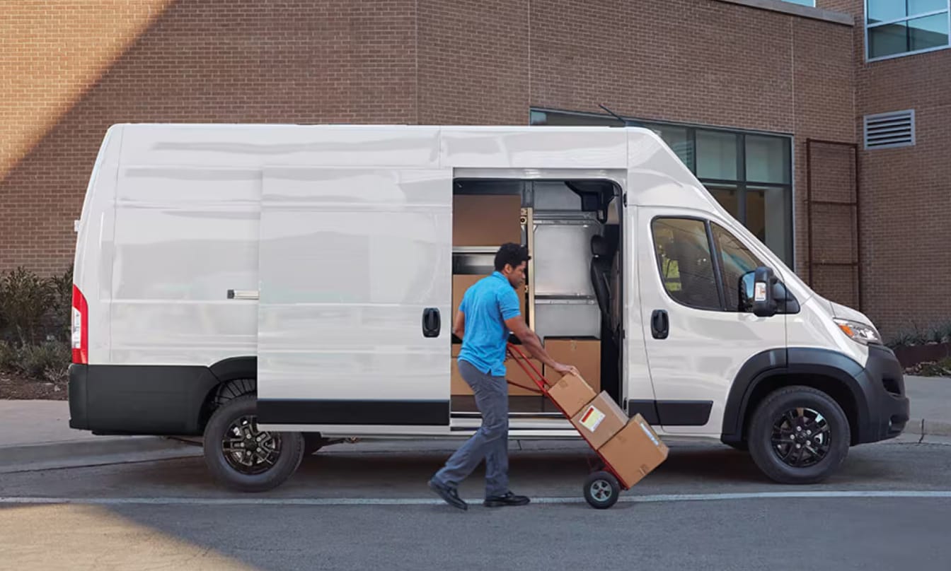 A man loads boxes into the side of a Ram Promaster 3500 with a dolly
