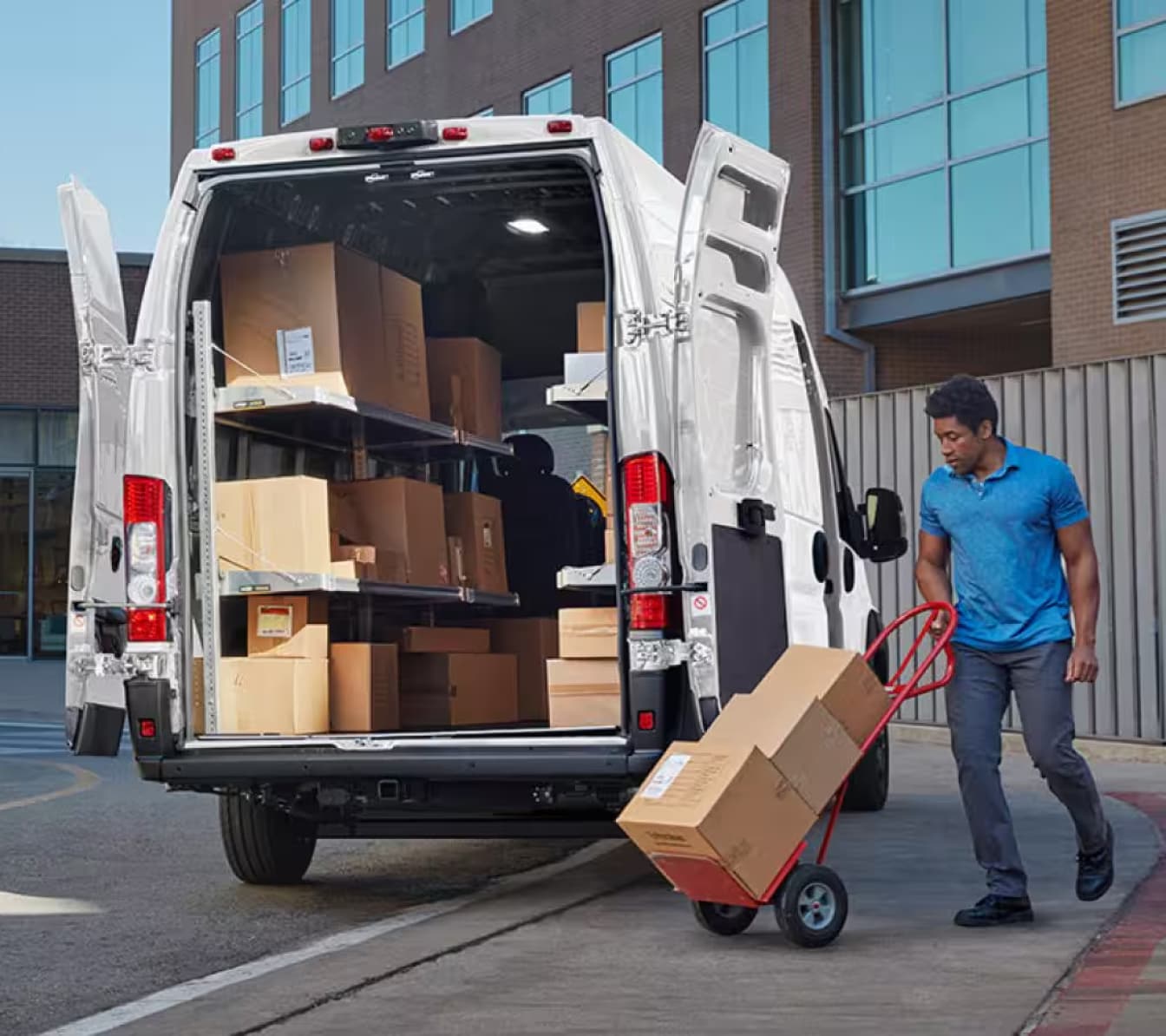 A man loads boxes into the back of a Ram Promaster 3500 with a dolly