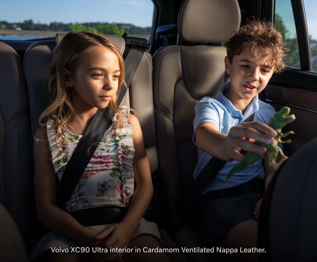 Rear passenger view of a Cardamom Ventilated Nappa Leather Volvo XC90 cabin with a boy and girl playing.