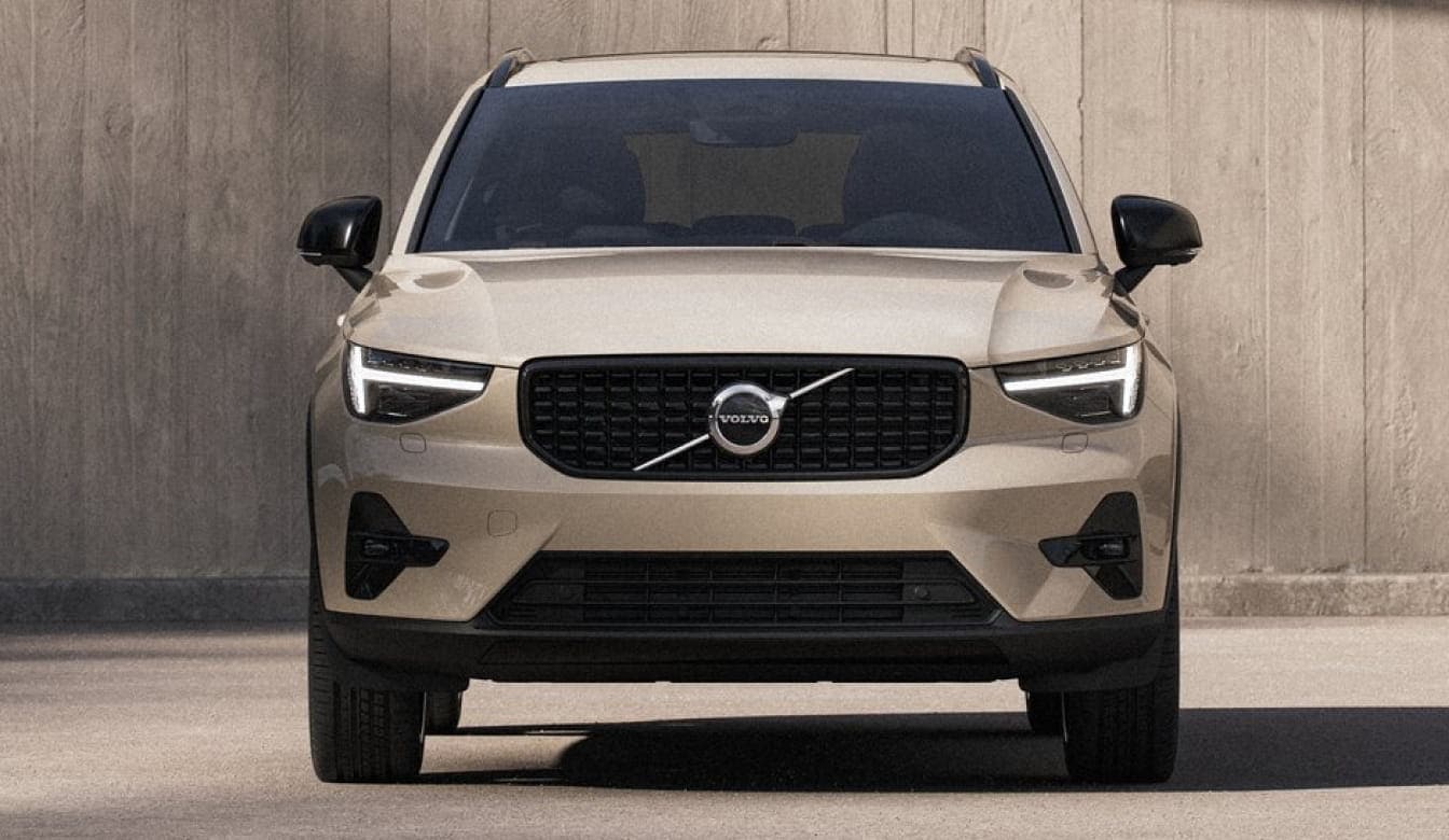 Front view of a beige Volvo XC40 with LED headlights and black grille against a concrete backdrop.