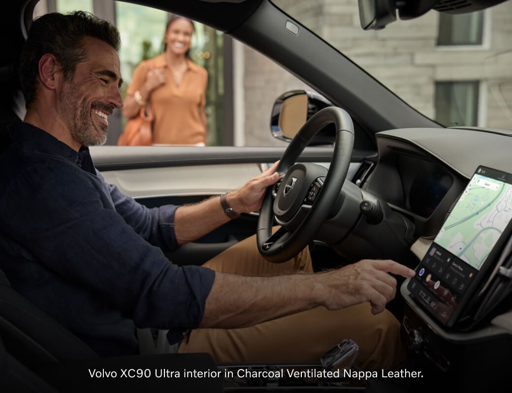 Interior view of a Charcoal Ventilated Nappa Leather Volvo XC90 cabin as a man uses the center touchscreen.