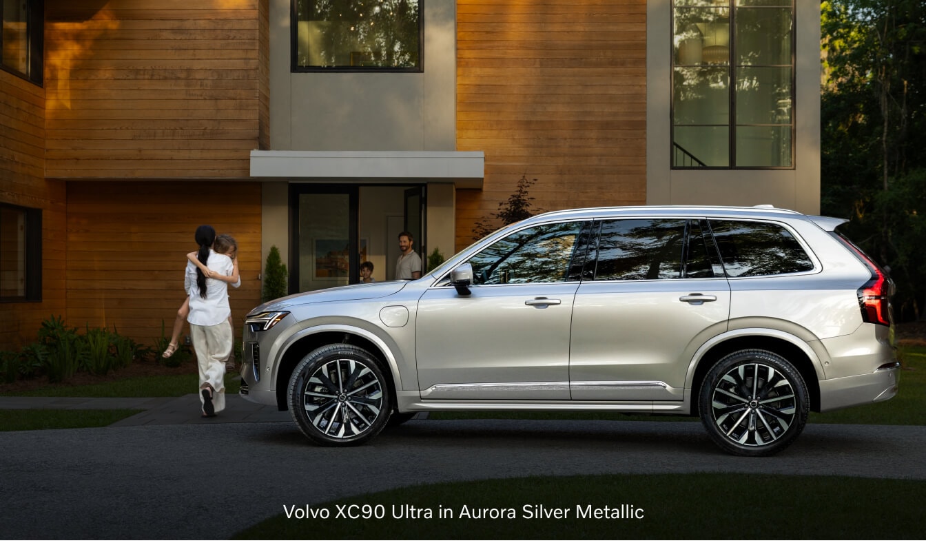 2026 Volvo XC90 Ultra profile view parked outside a modern home with a family.