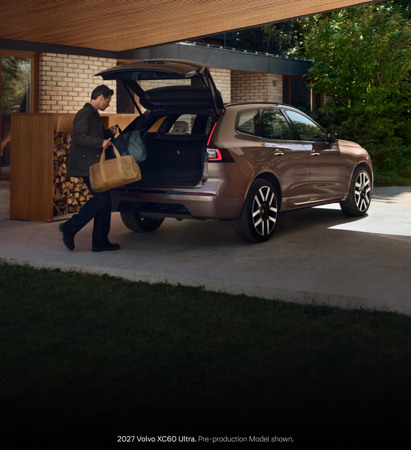 22027 Volvo XC60 Ultra in Heather Bronze parked under a modern residential carport with open tailgate as a man loads travel bags.
