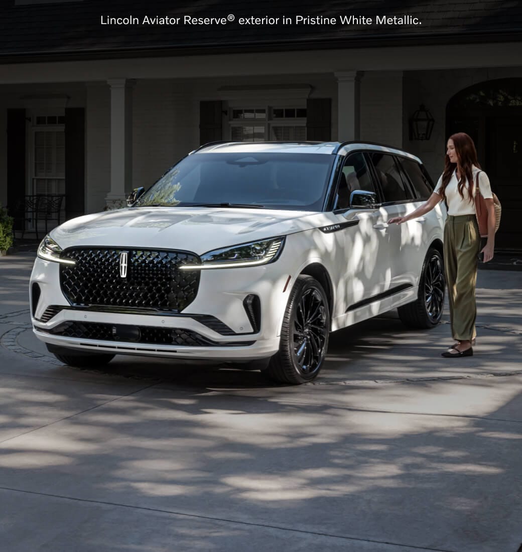 Three-quarter front view of a Pristine White Metallic Lincoln Aviator Reserve as a woman unlocks the driver door.