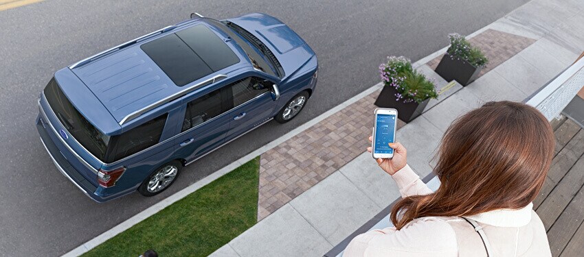 A young woman uses Ford Pass on her smartphone to unlock her New 2018 Ford Expedition from the second floor of an apartment.