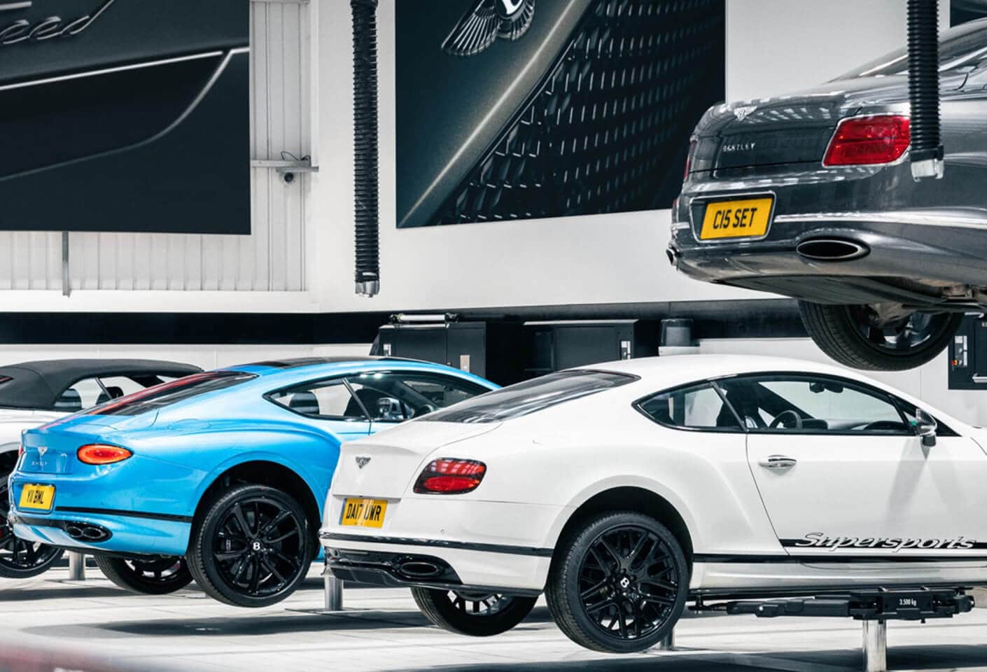 Interior view of luxury Bentley vehicles raised on hydraulic lifts inside a modern service center facility.