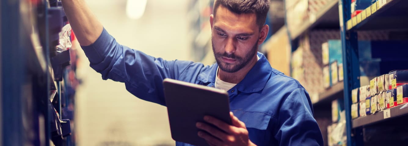 Technician using a tablet while checking automotive parts inventory in a service department.