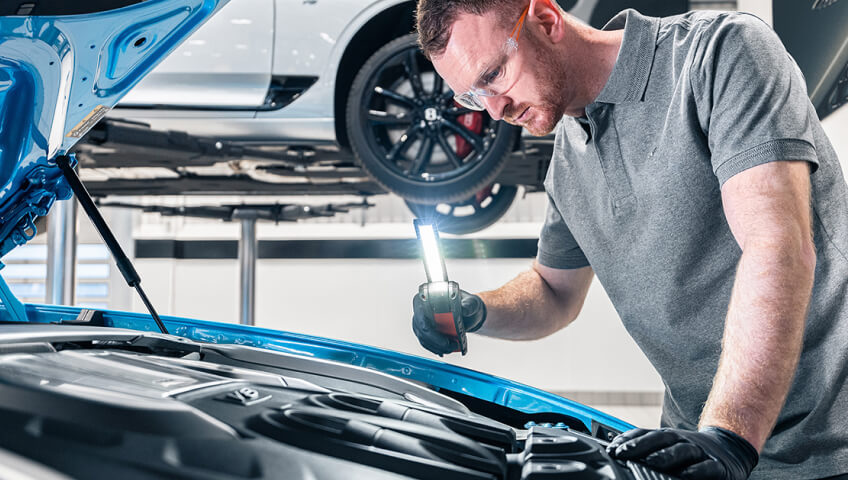 Close-up view of technician inspecting engine of bright blue Bentley in service bay.