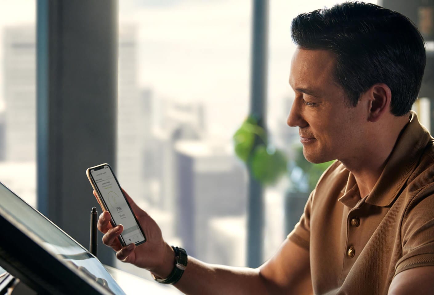 Side profile of a man using the official My Bentley smartphone app inside an office overlooking a city skyline.