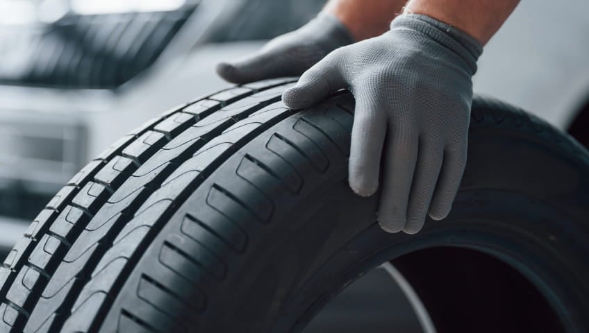 Technician wearing gloves inspecting the tread of a vehicle tire.