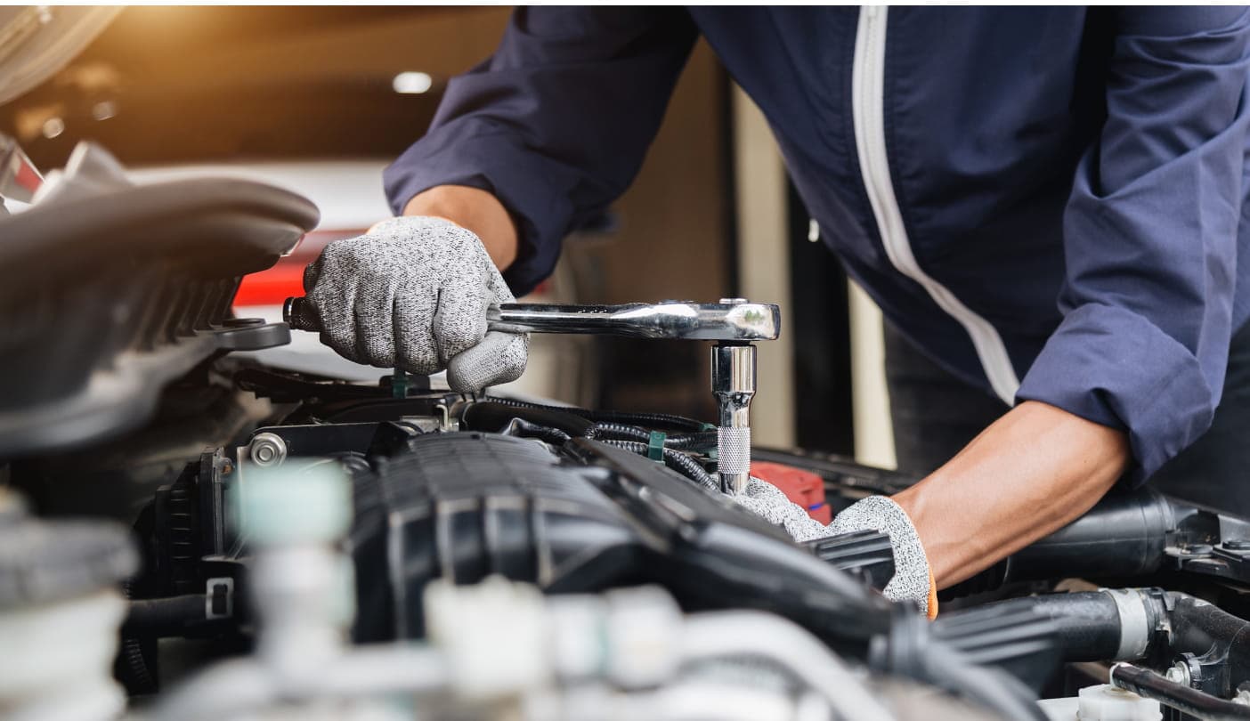 Technician using a ratchet wrench while performing maintenance in a vehicle engine bay.