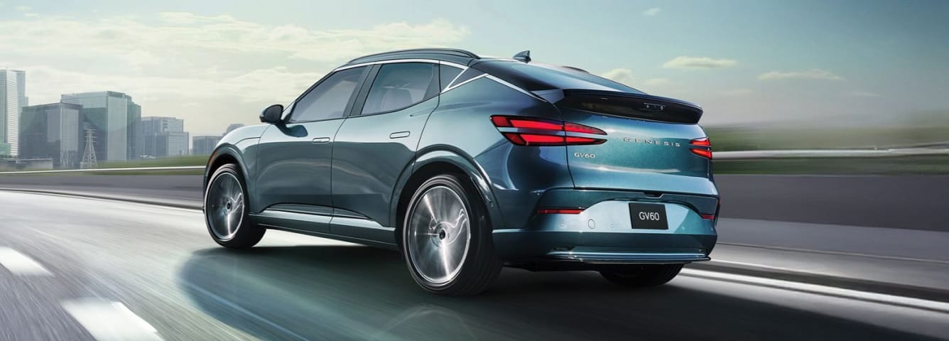 Genesis GV60 driving on a highway with a city skyline in the background.