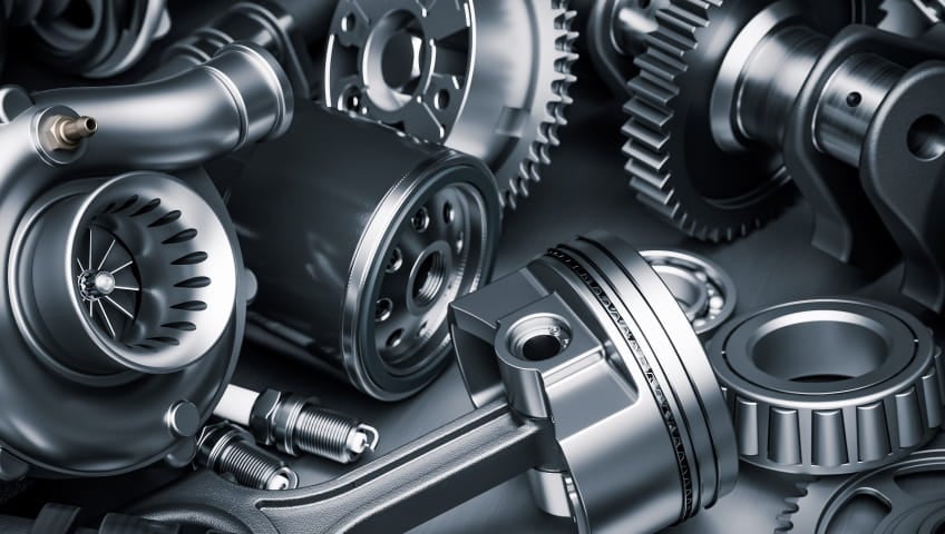 Close-up of automotive engine components, including gears, pistons, bearings, and spark plugs.