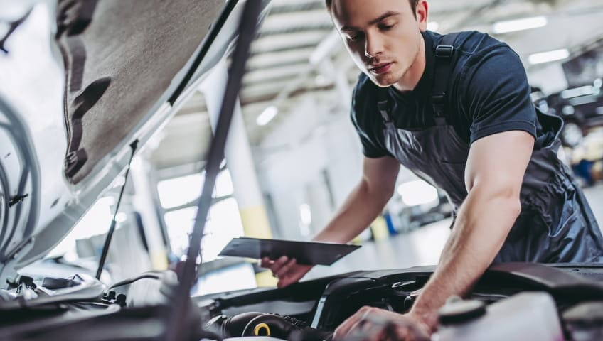Technician inspecting a vehicle engine while holding a diagnostic tablet.