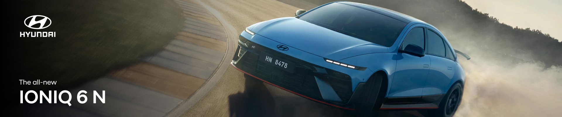 An exterior view of The all-new IONIQ 6 N taking a sharp turn on a hazy racetrack at golden hour.