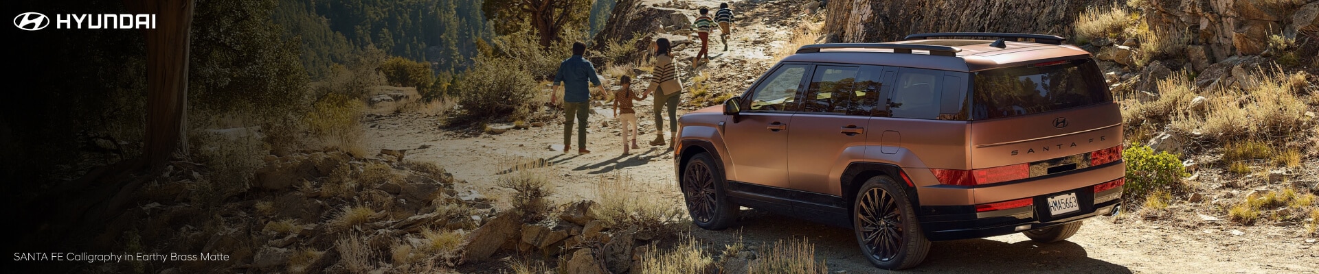 Family on an arid and rocky mountain with their 2026 Hyundai SANTA FE Calligraphy (in Earthy Brass Matte)