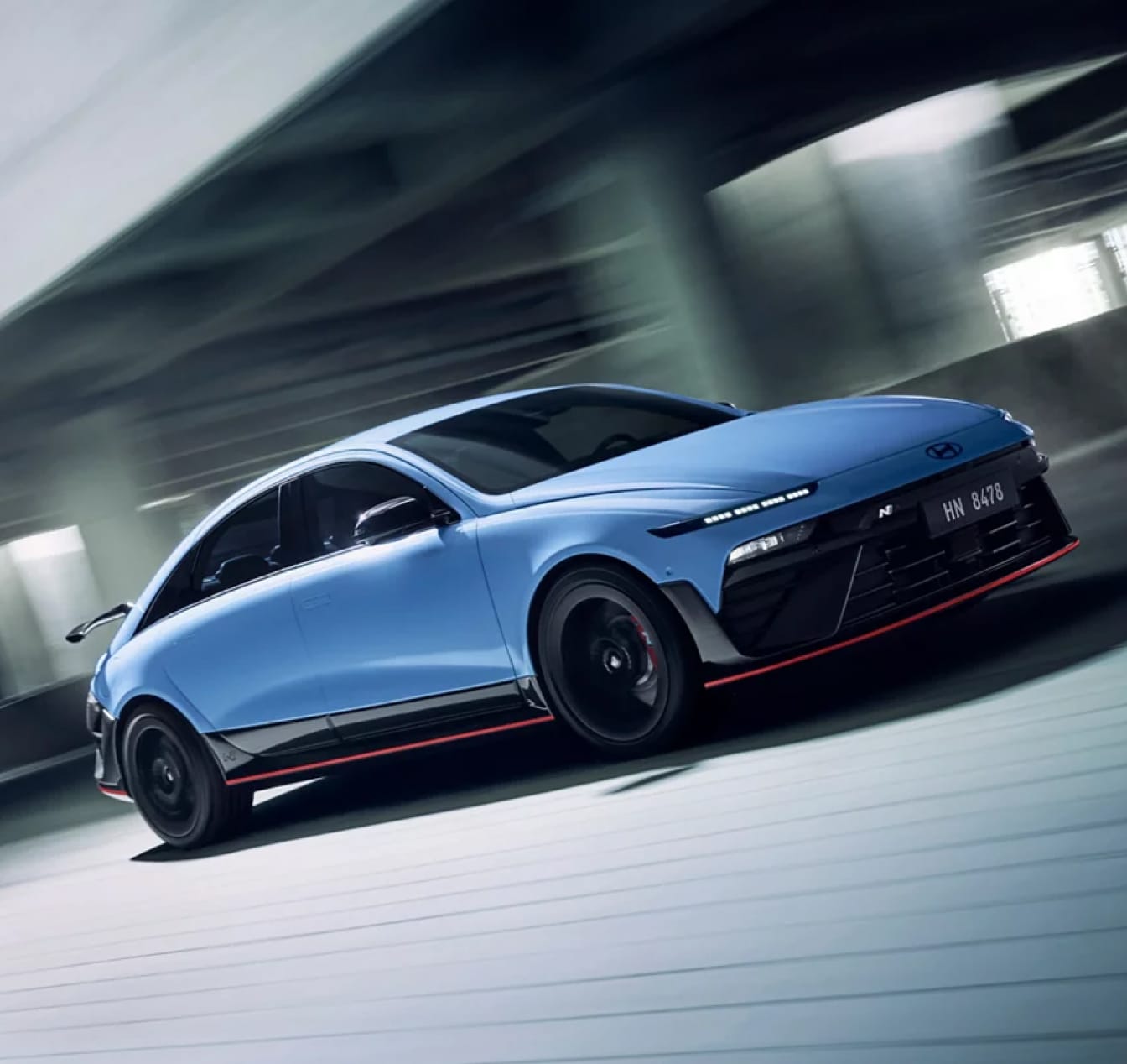 An exterior front three-quarter action shot of a blue Hyundai IONIQ 6 N speeding down a frontage road along an elevated highway.