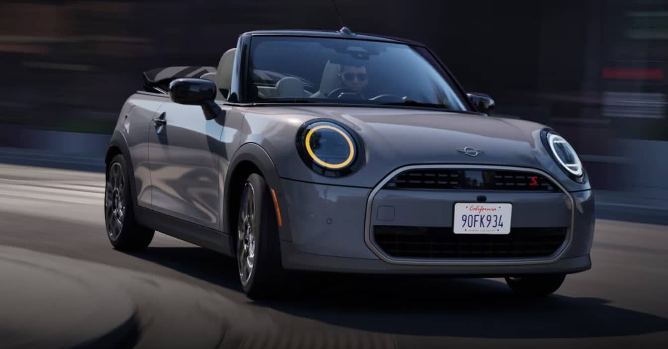 Front three-quarter view of a 2026 MINI Cooper S Convertible in Copper Grey Metallic driving along an open road.