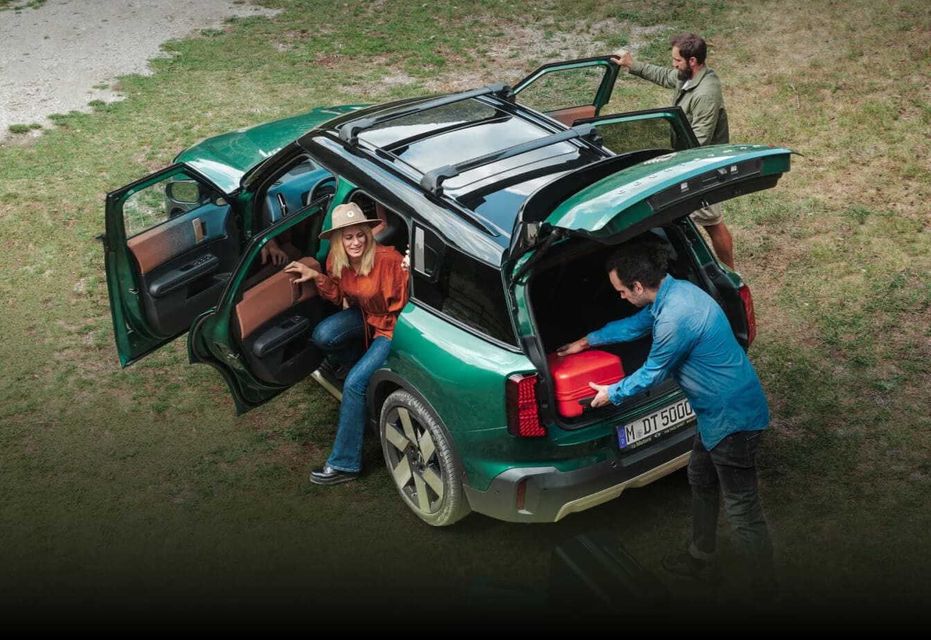 High-angle view of a 2026 MINI Countryman S ALL4 in British Racing Green IV Metallic with open doors and tailgate as a group of people loads luggage.