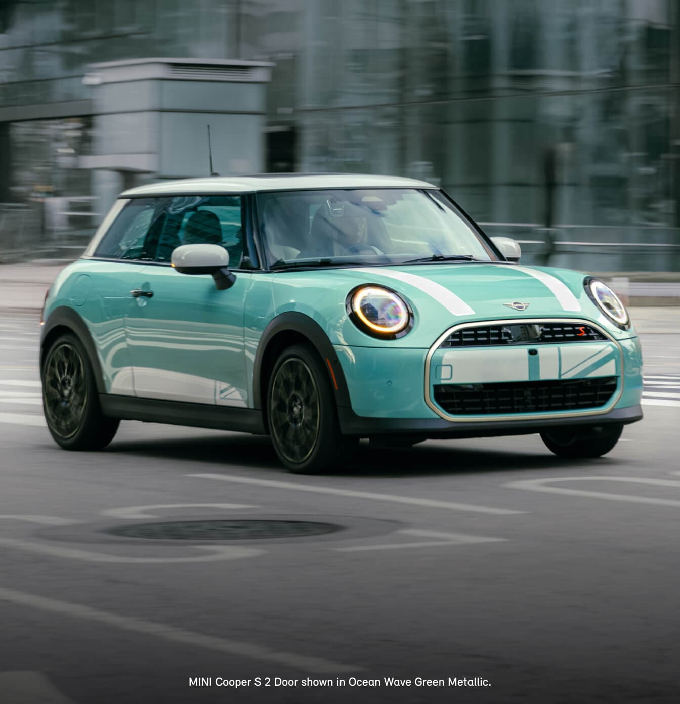Front three-quarter view of a 2026 MINI Cooper S 2-Door in Ocean Wave Green Metallic driving along a city street.
