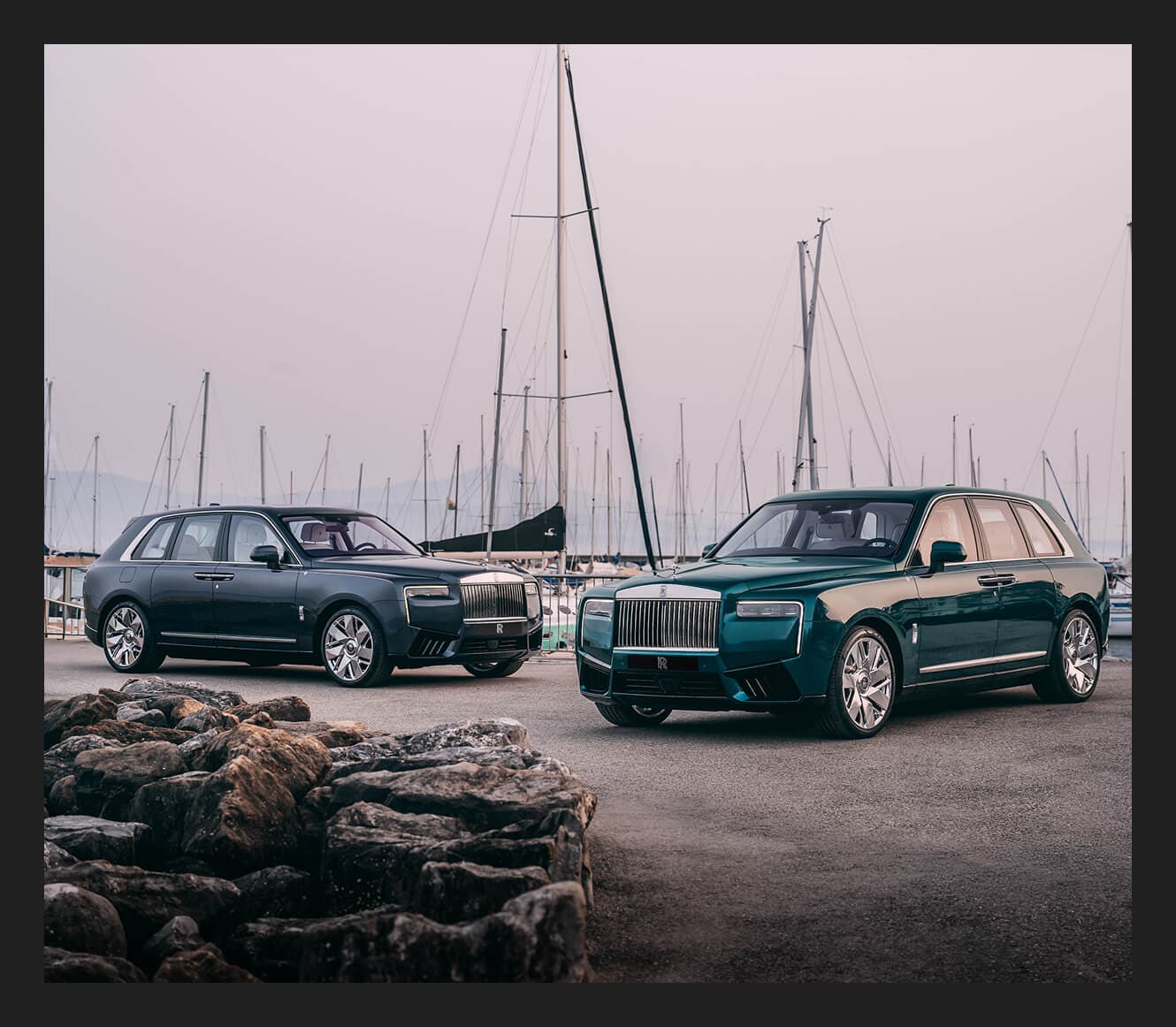 Front three-quarter view of a 2027 Rolls-Royce Cullinan Series II in blue and a 2027 Rolls-Royce Cullinan Series II in green parked before sailboats.