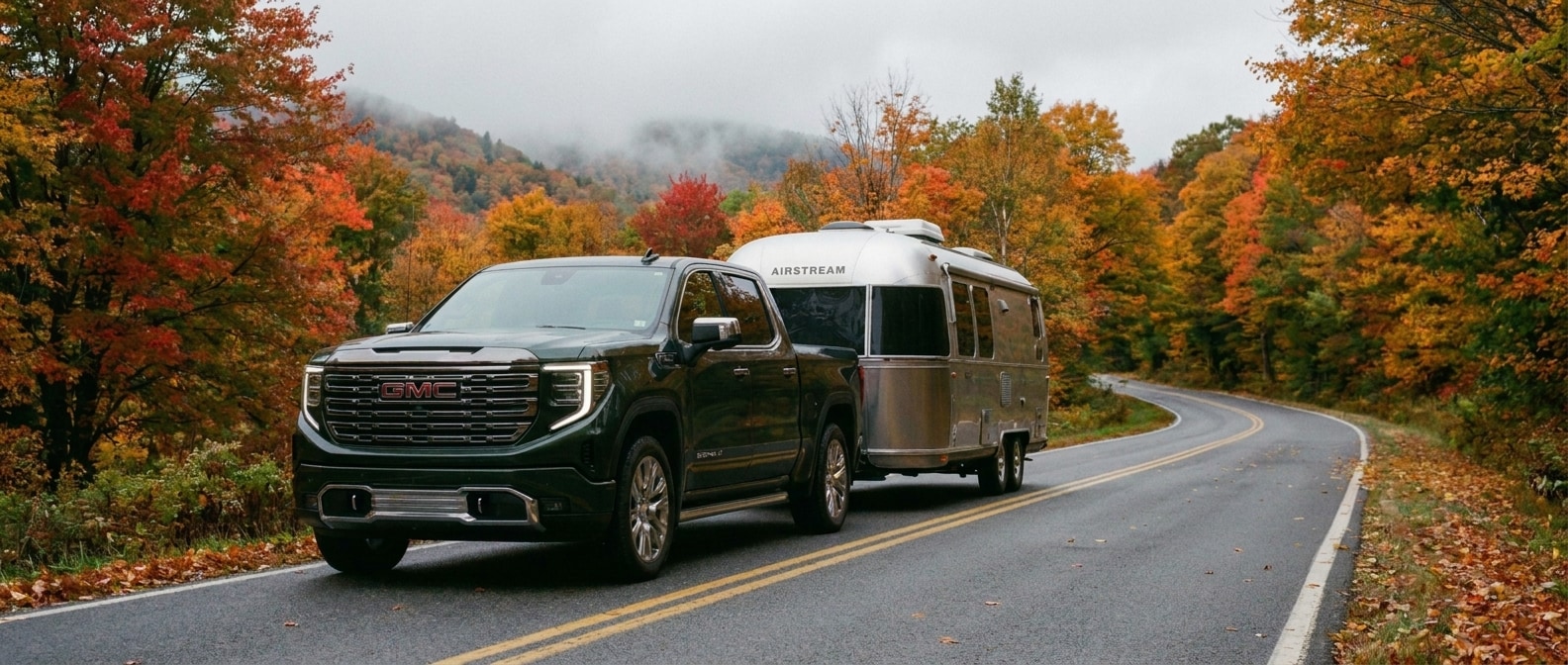 2026 GMC Sierra 1500 towing a travel trailer through Vermont fall foliage on a mountain road