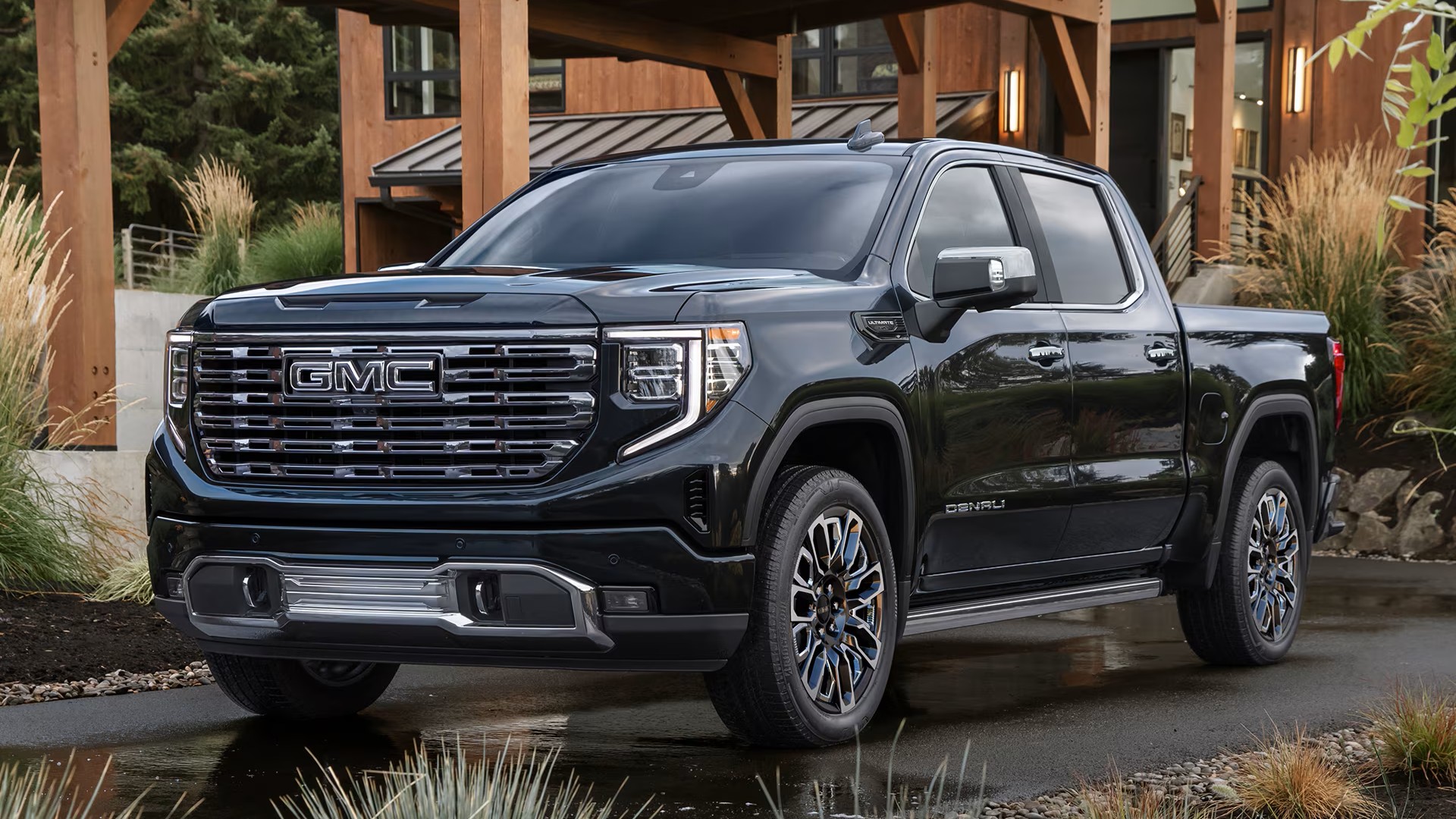 Black GMC Sierra 1500 Denali Ultimate in the previous-generation design, parked by a timber-frame house