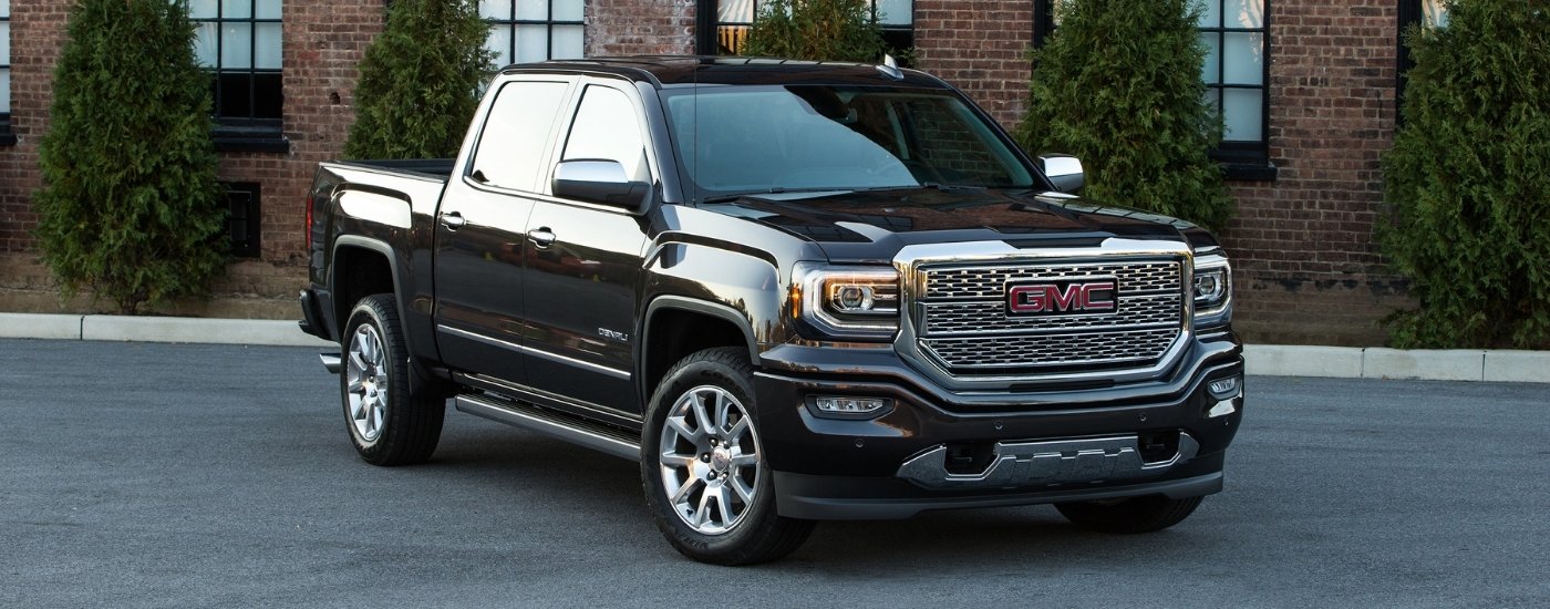 A black 2016 GMC Sierra 1500 Denali parked in front of a brick building.