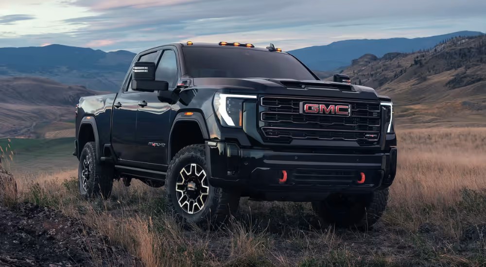 Black GMC Sierra HD heavy-duty pickup with amber roof marker lights in a grassy valley at dusk