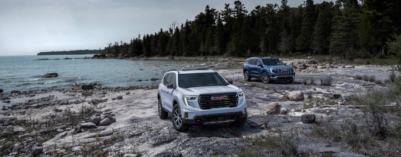 A white 2024 GMC Acadia AT4 parked next to a blue 2024 GMC Acadia Platinum