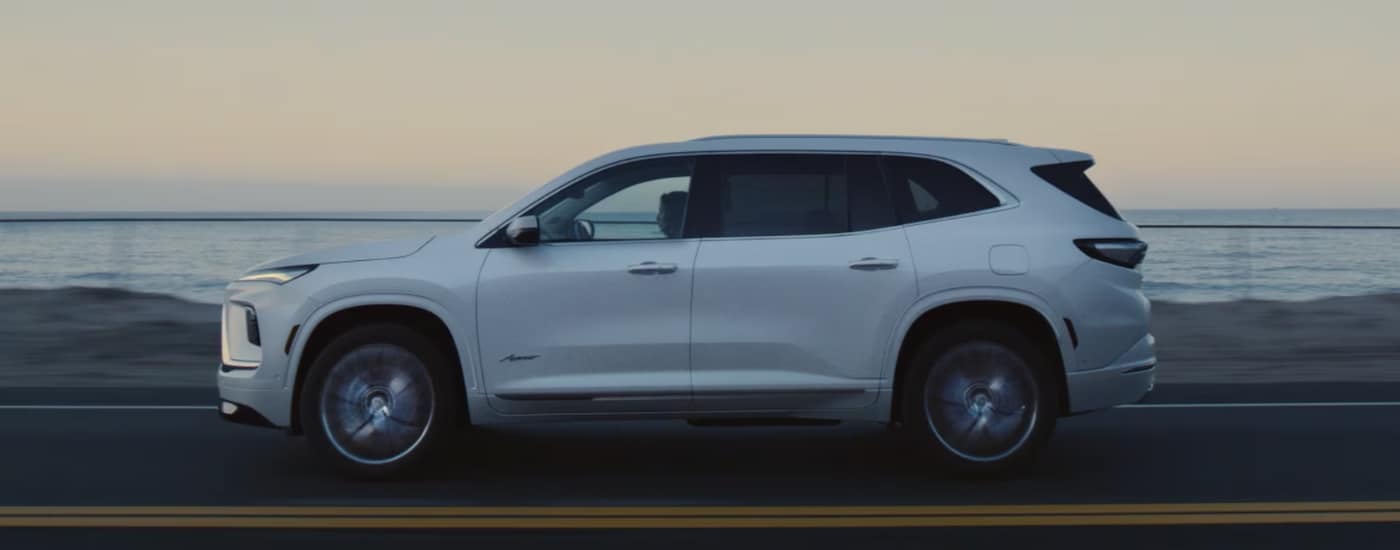 Side view of a white 2026 Buick Enclave driving on an open road