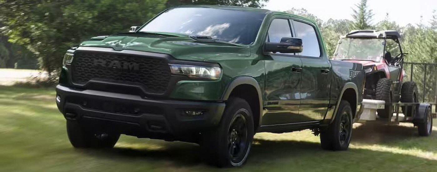 A green 2026 Ram 1500 towing a trailer on grass.