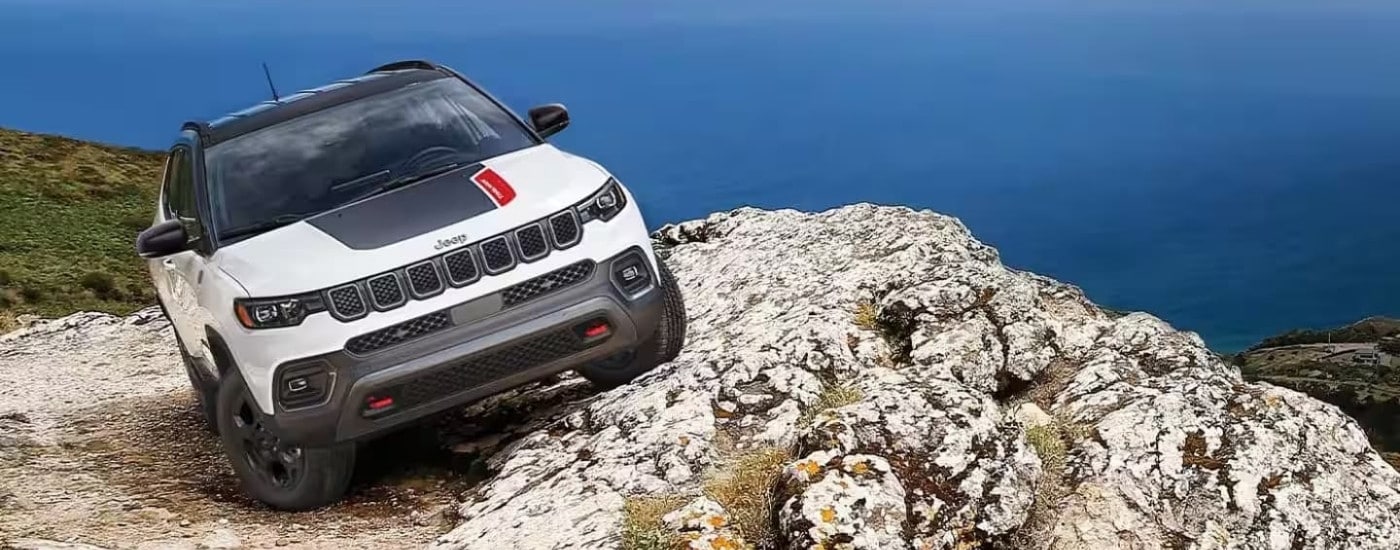 A white 2023 Jeep Compass Trailhawk is parked off-road.