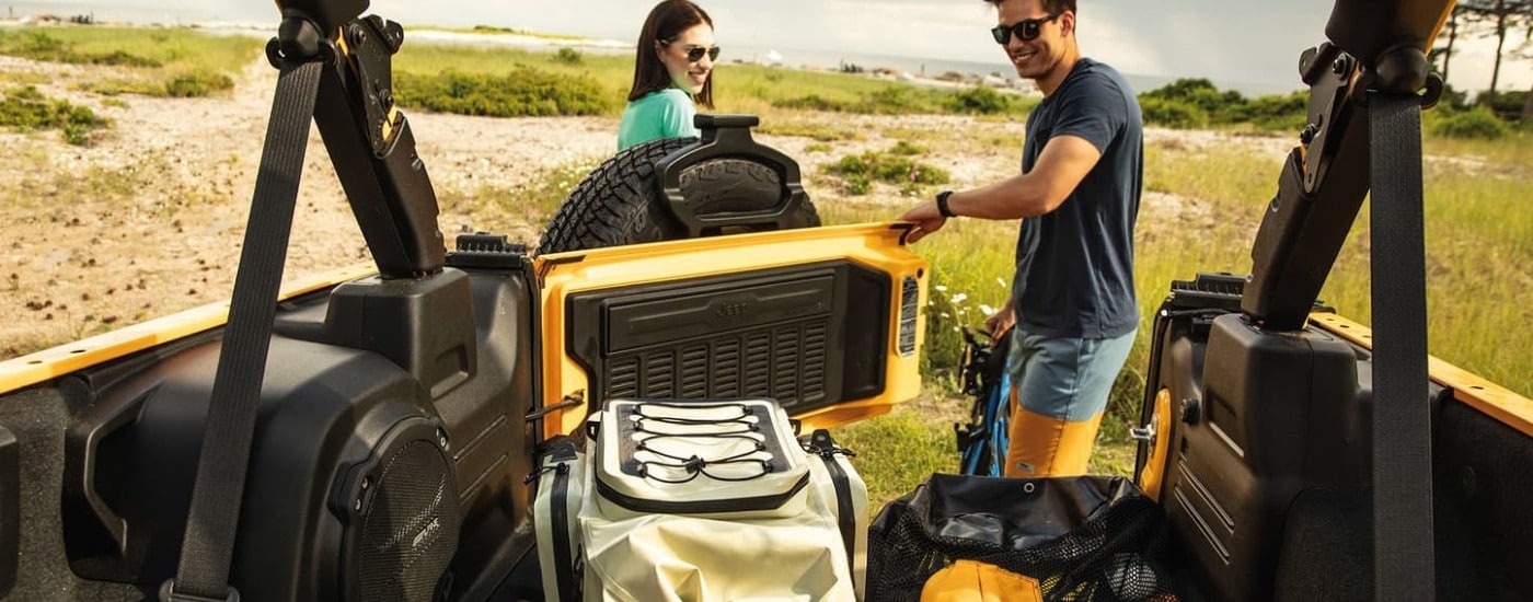 A person opening the trunk of a yellow 2021 Jeep Wrangler.