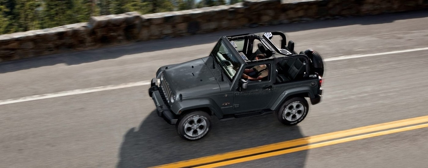 Grey 2017 Jeep Wrangler Sahara driving past a stone wall