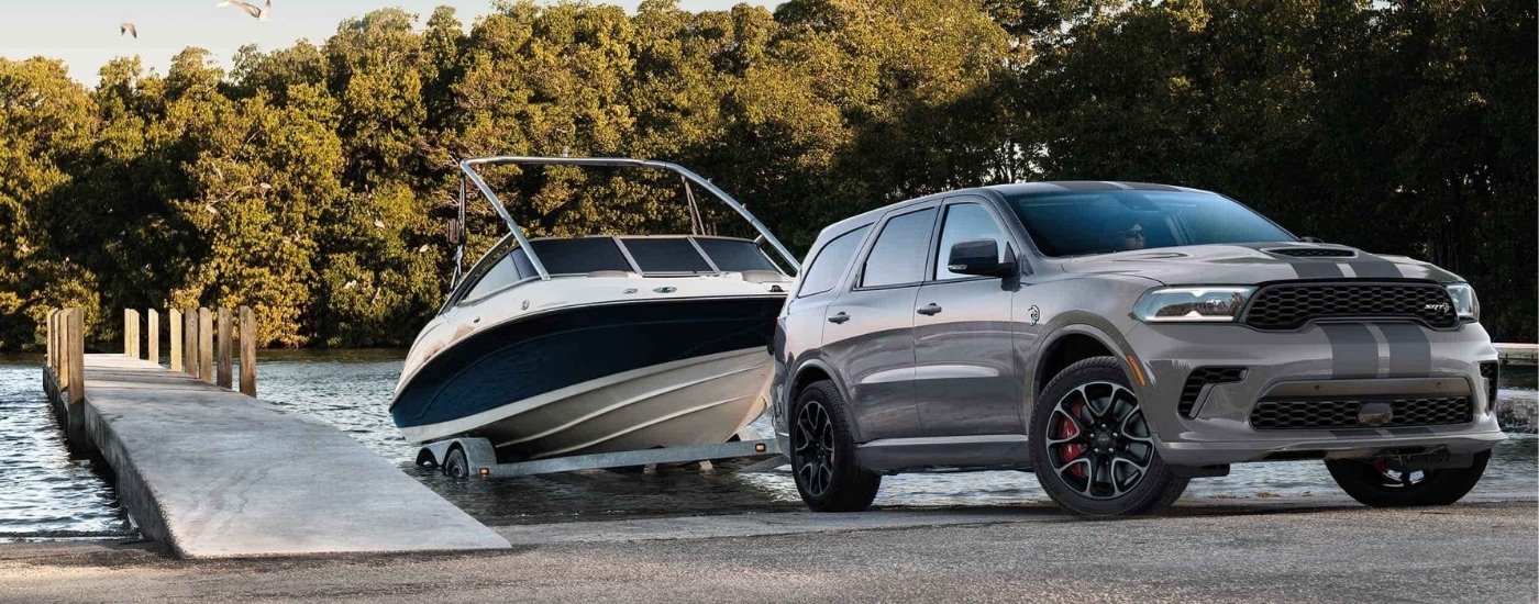 A grey 2024 Dodge Durango SRT Hellcat is towing a boat near a dock.