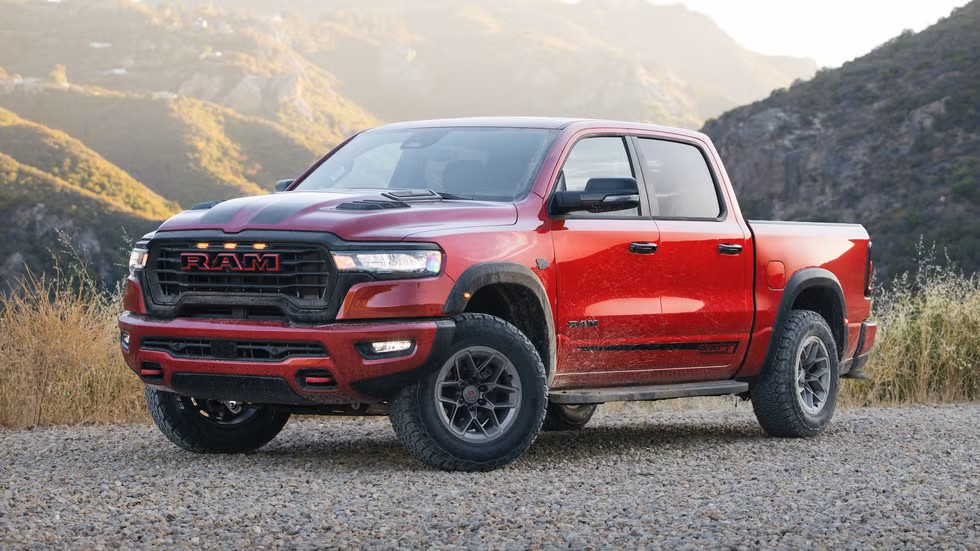 Red Ram 1500 crew cab with off-road tires parked on gravel, front three-quarter view, hills behind