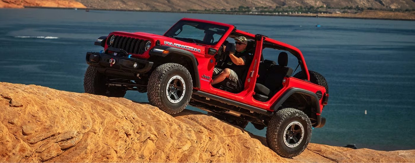 A red 2025 Jeep Wrangler 4xe Rubicon is driving to a Jeep dealer.