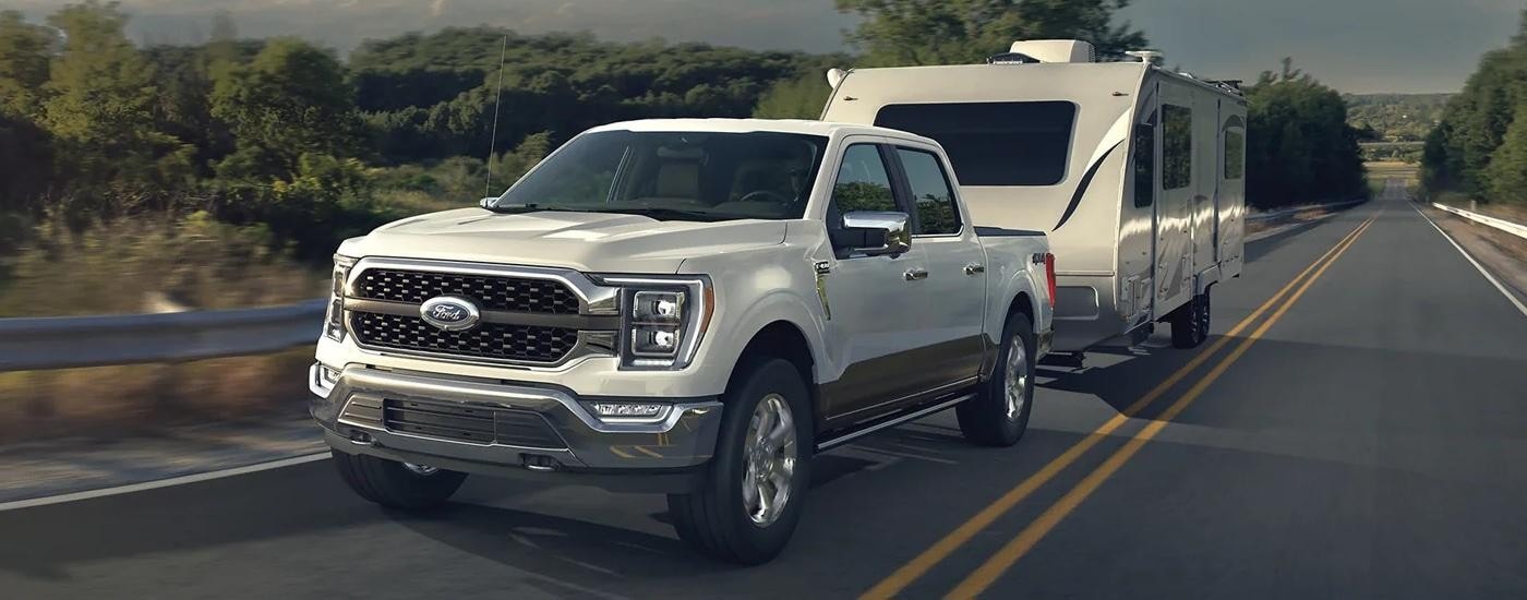 White 2023 Ford F-150 towing a camper trailer on a highway