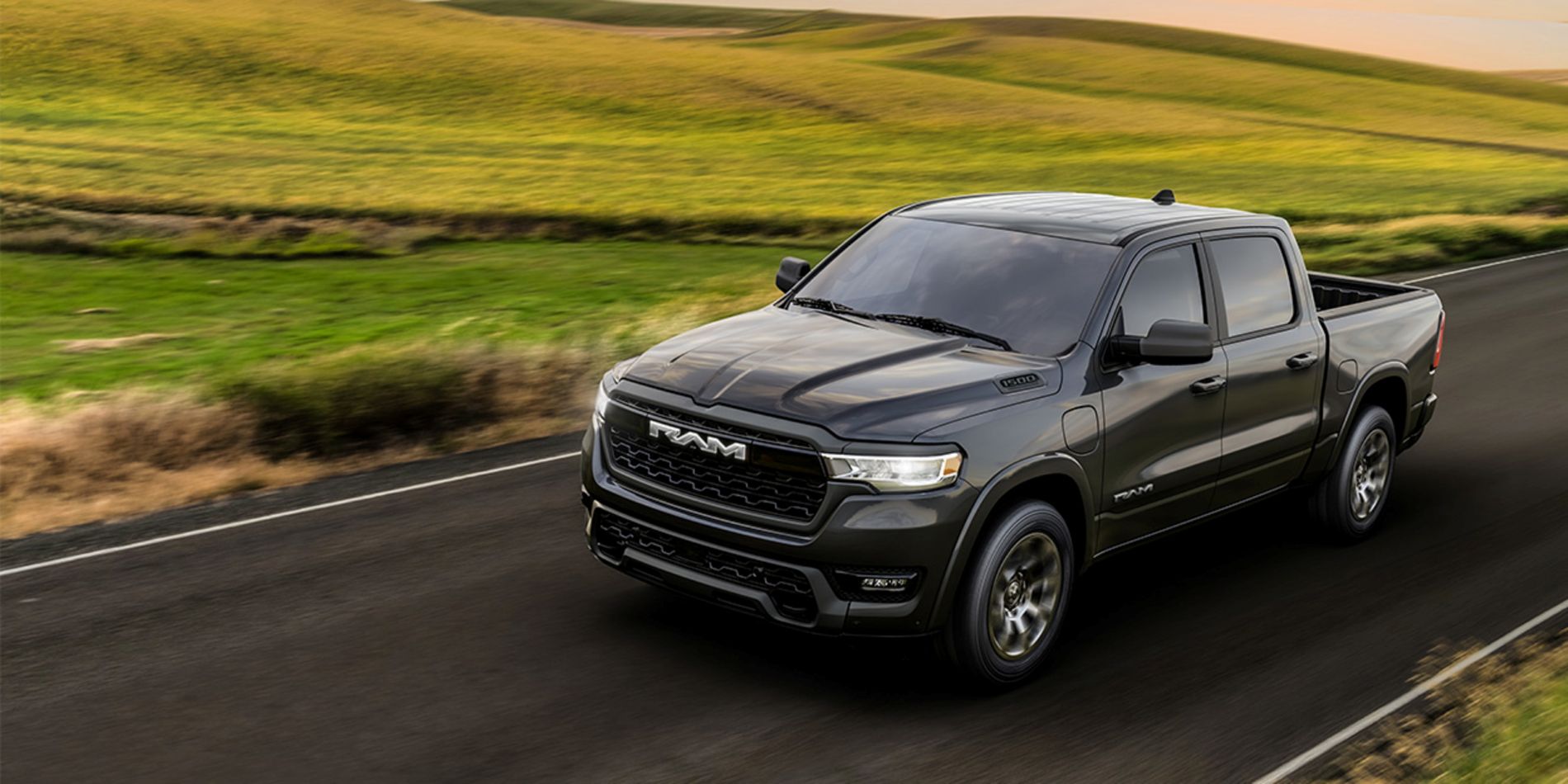Dark gray Ram 1500 crew cab driving on a two-lane road through green rolling hills