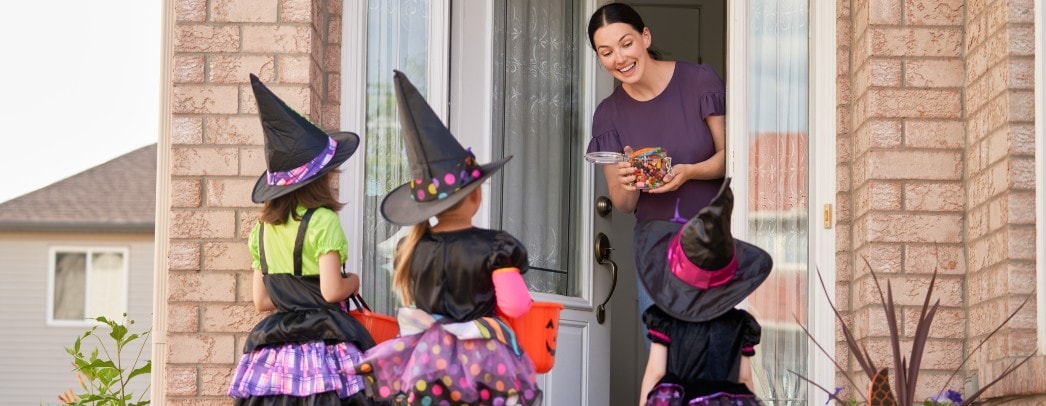 Woman Handing Candy to Three Trick or Treaters on Halloween