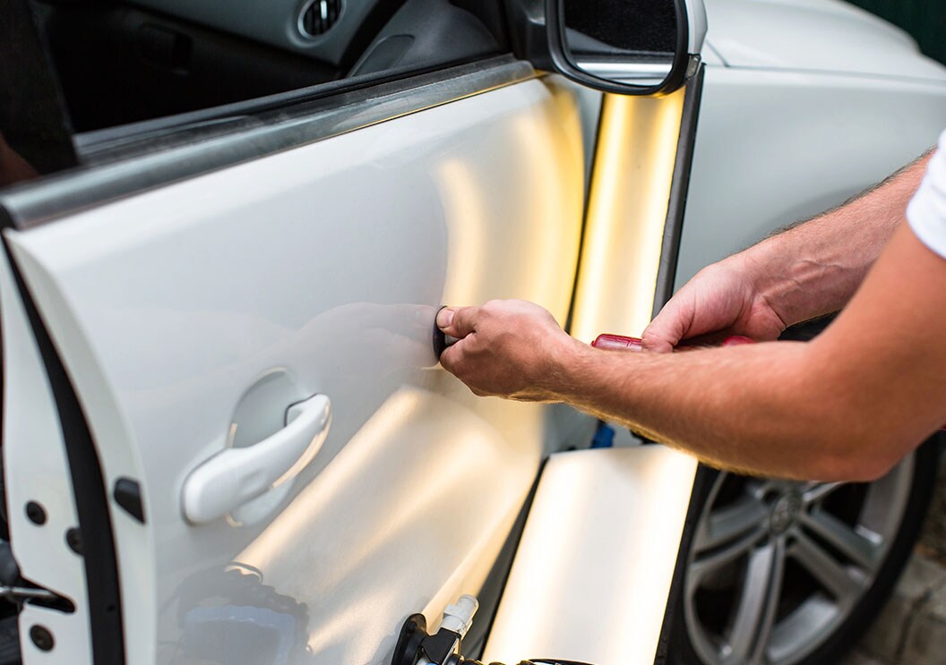 Technician using specialized tools and reflection lighting to perform paintless dent repair on a vehicle door
