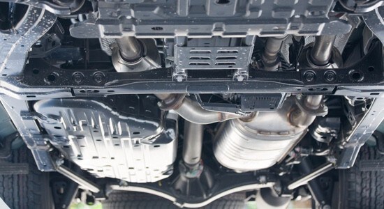 View beneath a vehicle showing undercarriage panels, exhaust, suspension, and structural components