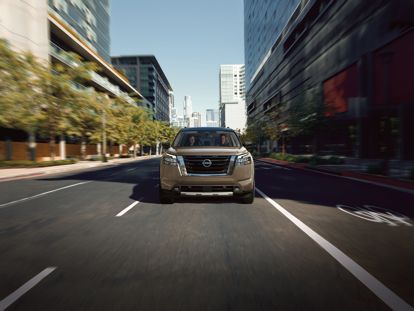  Man and woman driving a 2025 Nissan Pathfinder down a city street.