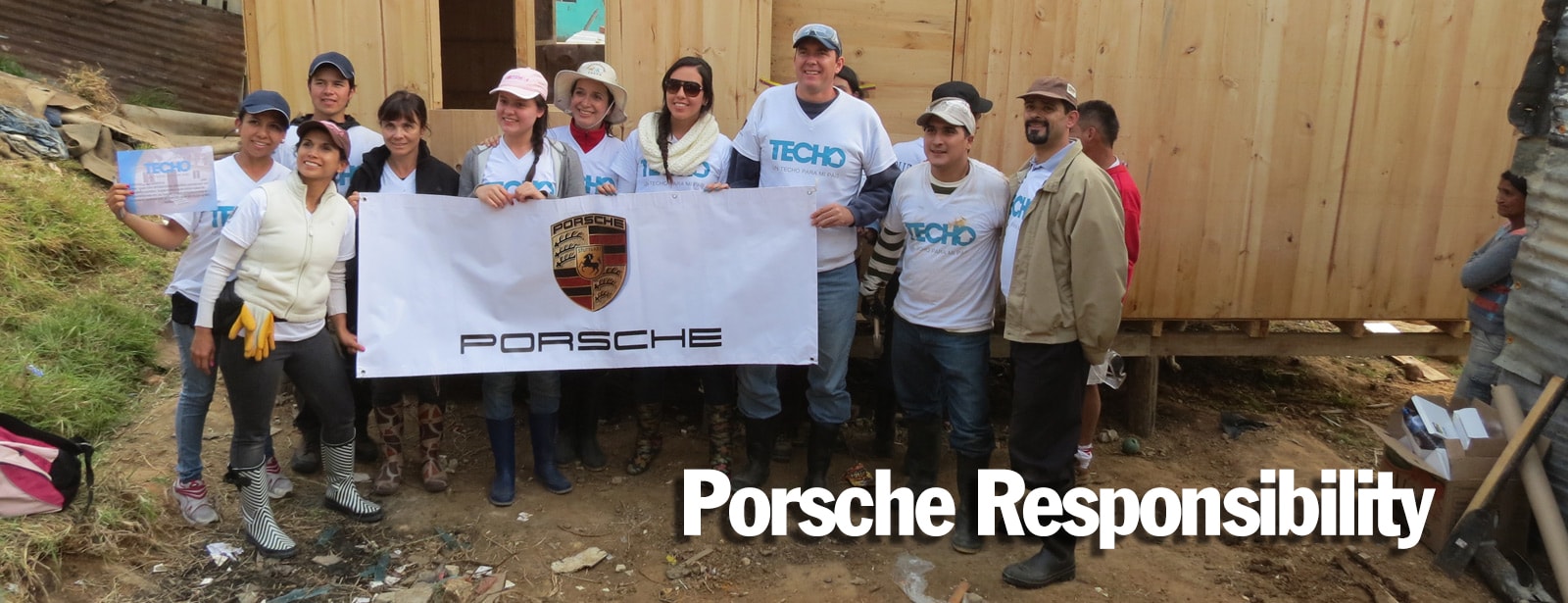 Porsche Responsibility page banner | A group of people who helped build a house, standing together and holding a Porsche banner