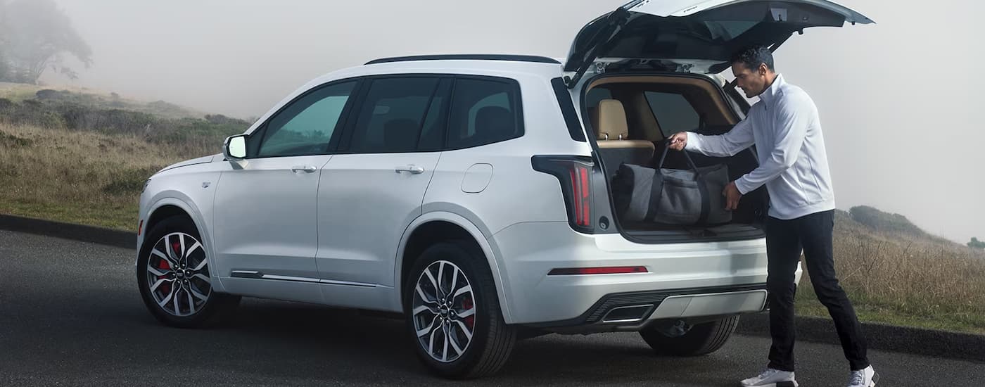A man is shown putting luggage into the back of a white Cadillac XT6 parked on a foggy road.