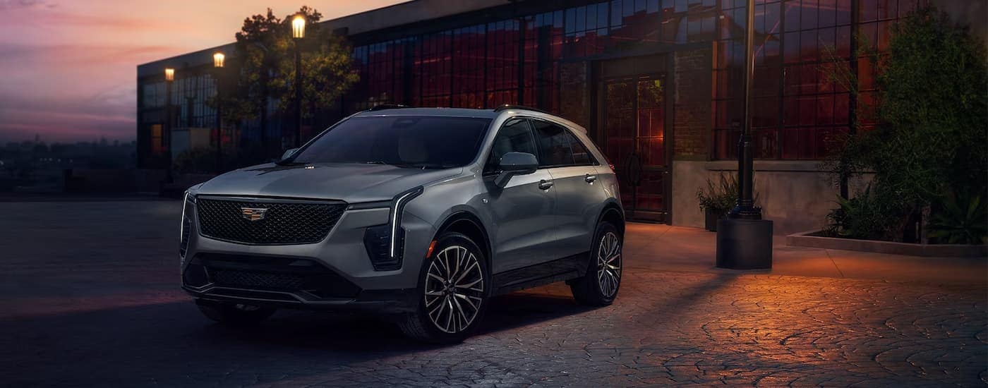 A silver 2024 Cadillac XT4 is shown parked at night in front of a restaurant.
