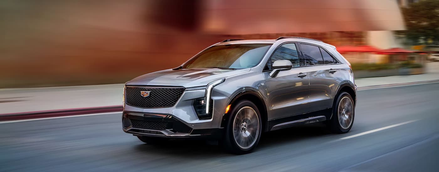 A silver 2025 Cadillac XT4 is driving on a city street with a blurred background.