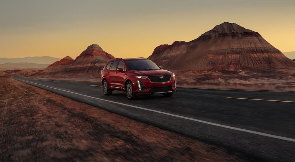 A red 2025 Cadillac XT6 is shown driving on a highway.
